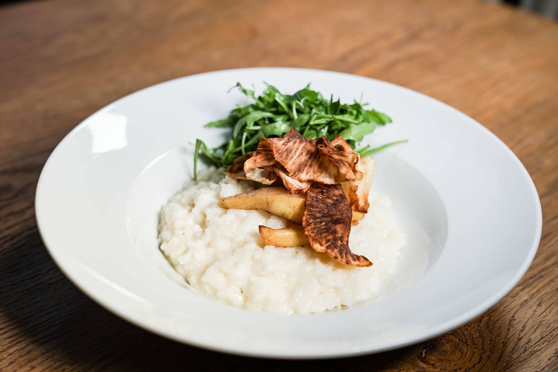 Risotto Wiener Küche Café Diglas Wien 1010 - Cremiges Risotto mit Rucola und knusprigen Chips auf weißem Teller